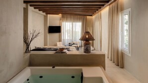 A modern bathroom with a large bathtub, a seating area with a sofa and a table, and a TV mounted on the wall. - Tesoro Elegant escapes-suites (Naxos)