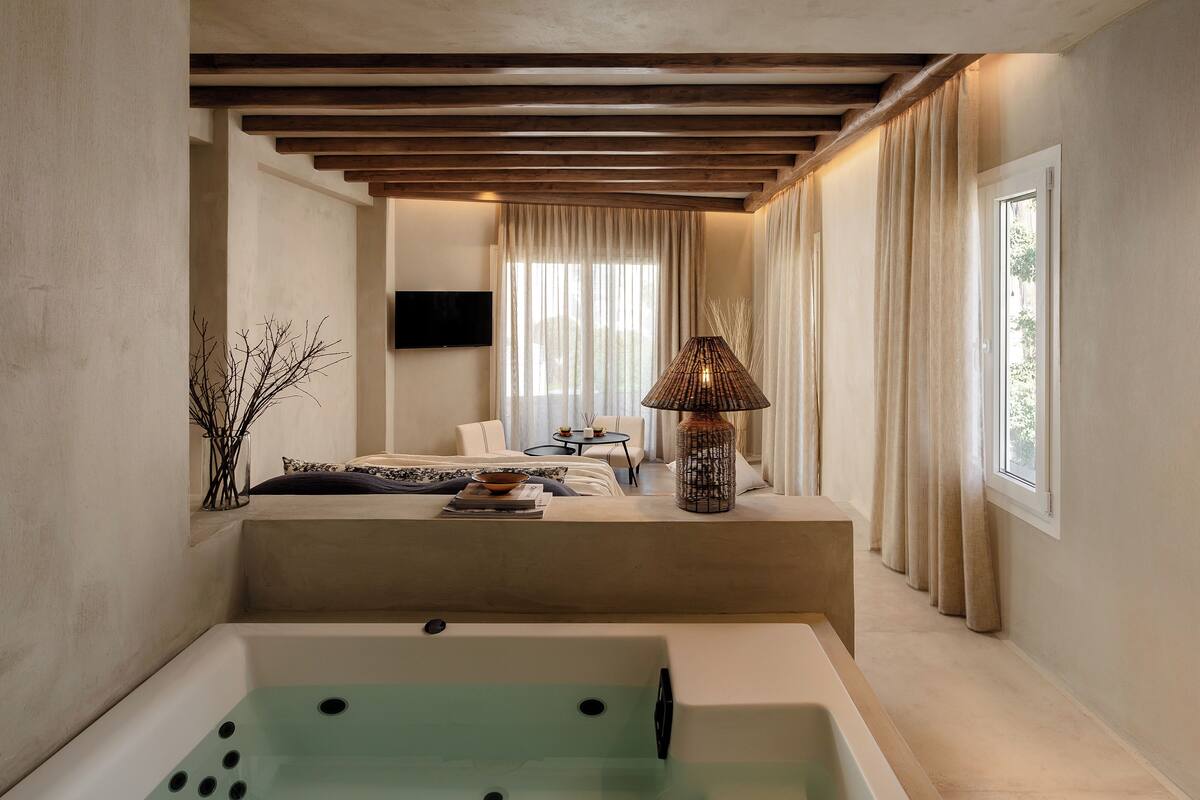 A modern bathroom with a large bathtub, a seating area with a sofa and a table, and a TV mounted on the wall.