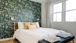 A bedroom with a floral wallpaper, a bed with white bedding, a bedside table with towels, and a window with curtains. - Cuyahoga Valley National Park, Hiking,Dog Friendly (Brecksville)