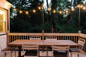 Una terraza de madera con una mesa y sillas, rodeada de luces colgantes y árboles.