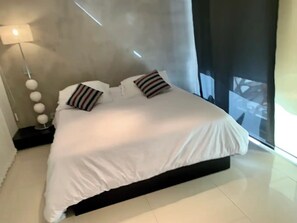 Relax in this serene bedroom with a large bed, floor-to-ceiling window, and stylish floor lamp.