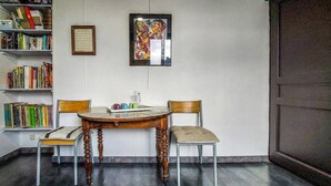 A room with a round wooden table, two chairs, a bookshelf, and a framed artwork on the wall.