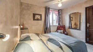 A bedroom with a bed, a ceiling fan, a window with curtains, a chair, and a mirror.