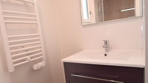 Un baño con lavamanos blanco, tocador oscuro, espejo y toallero.