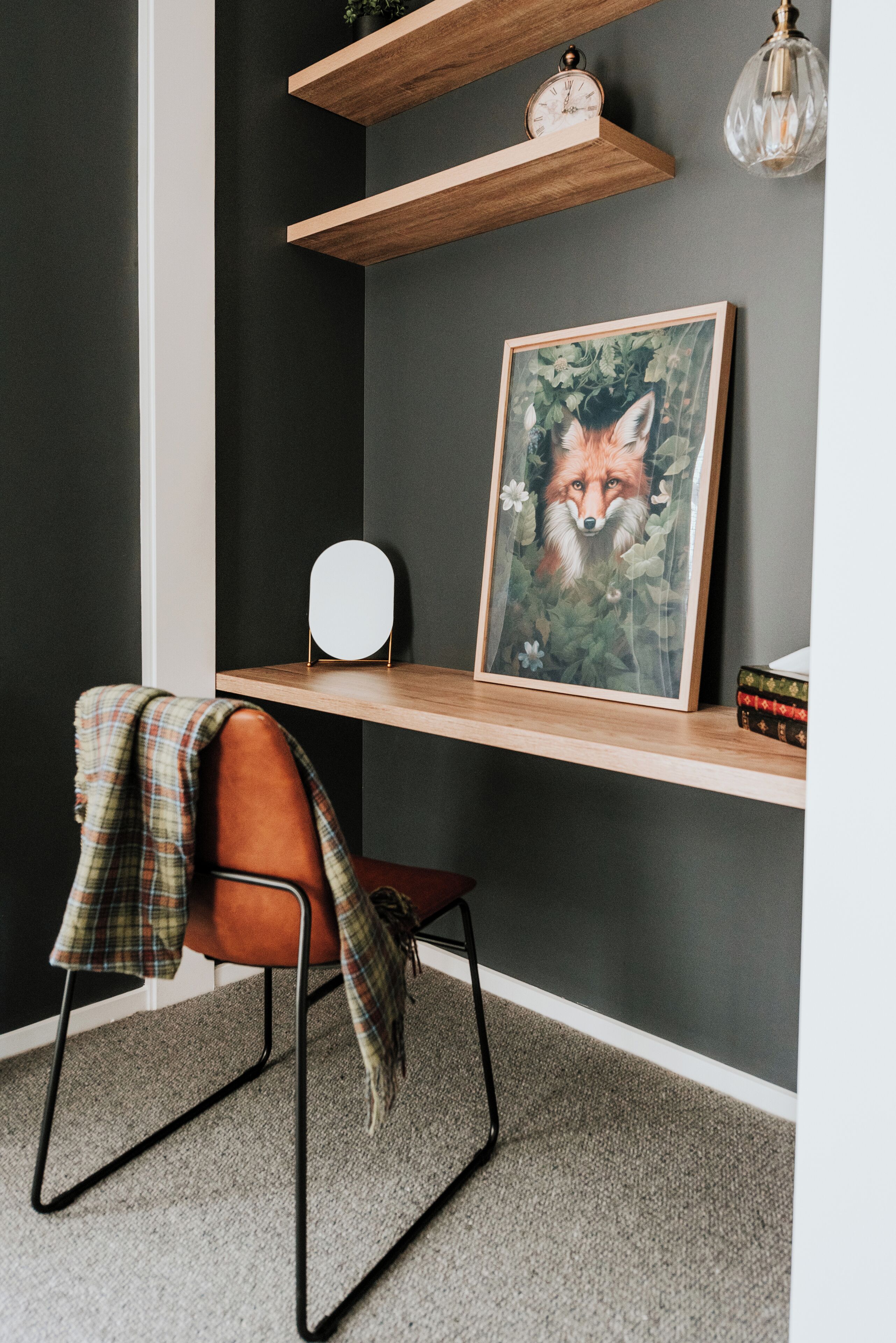 A modern room with a dark grey wall, a wooden desk with a framed picture, a clock, and a hanging light fixture.