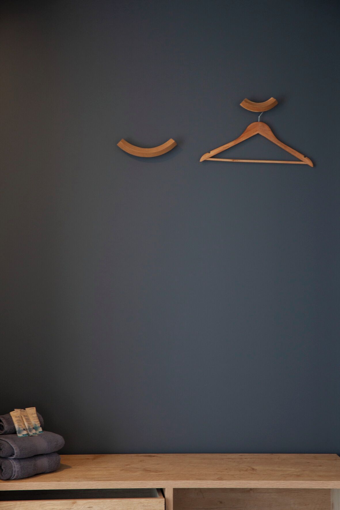 A dark blue wall with a wooden hanger and a wooden hanger with a curved hook.