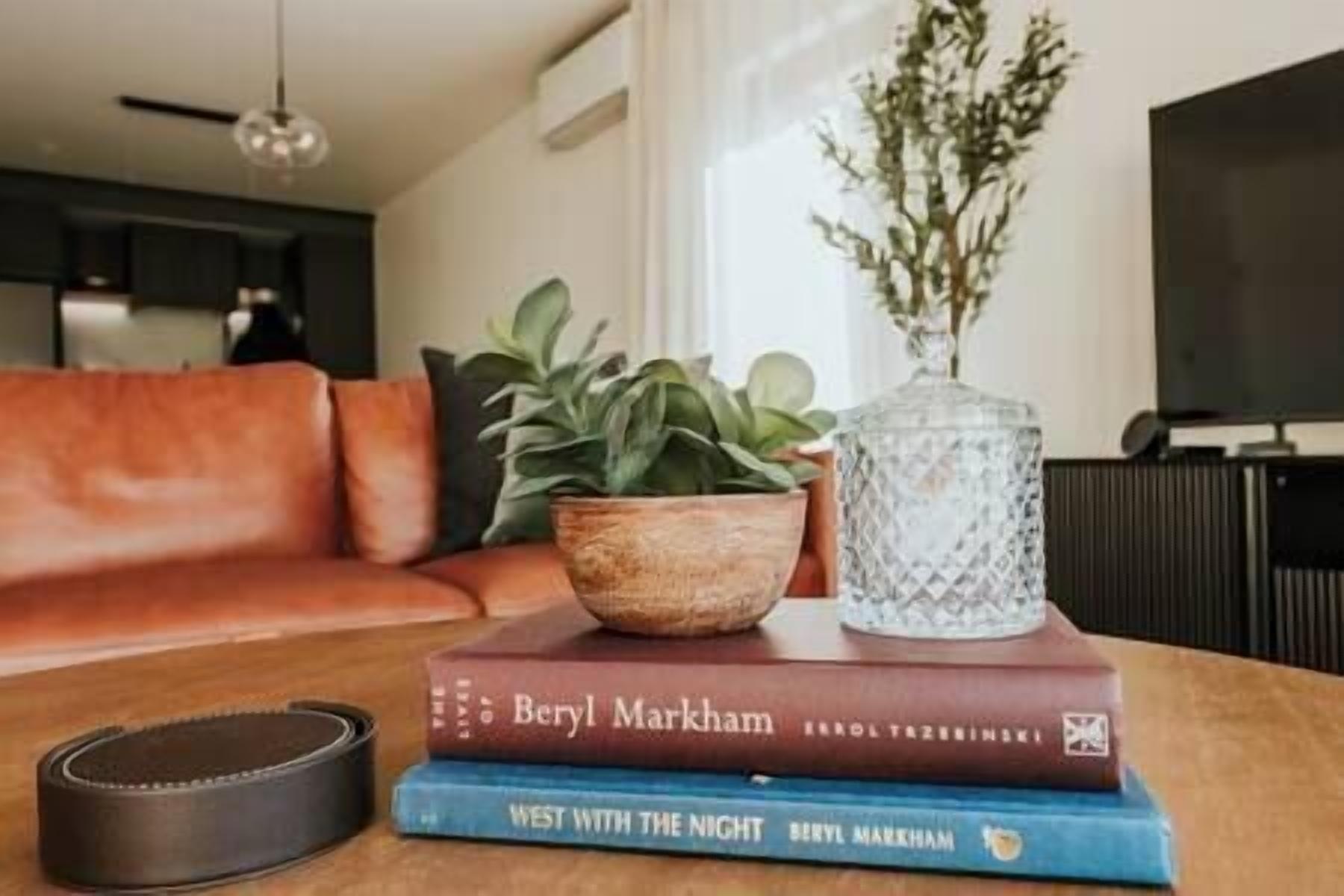 A living room with a sofa, a coffee table, a plant, and two books titled 'West With The Night' by Beryl Markham.
