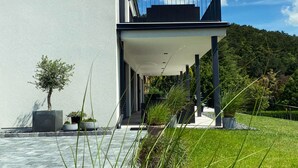 Un bâtiment moderne doté d’un toit plat, d’un espace extérieur couvert et d’un jardin verdoyant.