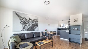Un salon moderne avec un canapé en cuir noir, une table basse en bois et une grande œuvre d’art en noir et blanc représentant la Tour Eiffel.
