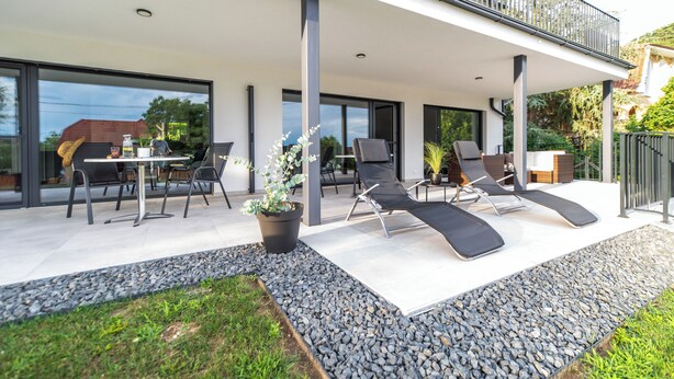 Une terrasse extérieure moderne comprenant un espace repas, des fauteuils et un pot de fleurs.