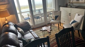 A living room with a leather sofa, a wooden chair, a white cabinet, and a view of a balcony with outdoor furniture.