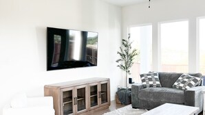 Un saló modern amb televisió de pantalla plana, ventilador de sostre, moble de fusta, sofà gris i taula de cafè blanca.