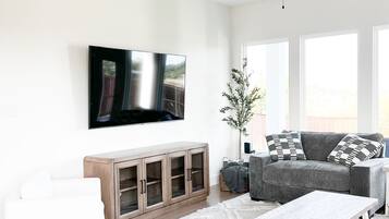 A modern living room with a flat-screen TV, a ceiling fan, a wooden cabinet, a grey sofa, and a white coffee table.