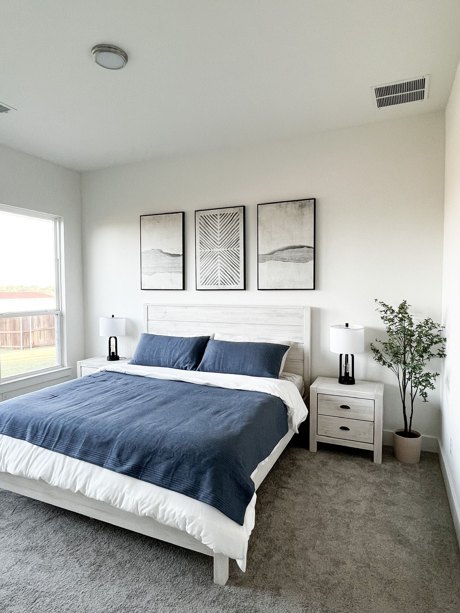A bedroom with a bed, bedside tables, a potted plant, and artwork on the wall.
