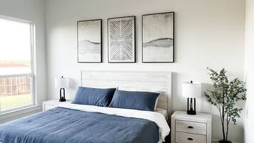A bedroom with a bed, bedside tables, a potted plant, and artwork on the wall.