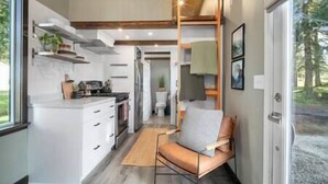 Una cocina compacta con armarios blancos, horno integrado y un comedor con una silla de cuero marrón.