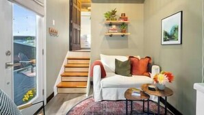Una sala de estar moderna con un sofá blanco, una mesita redonda y una escalera que lleva a otro nivel.