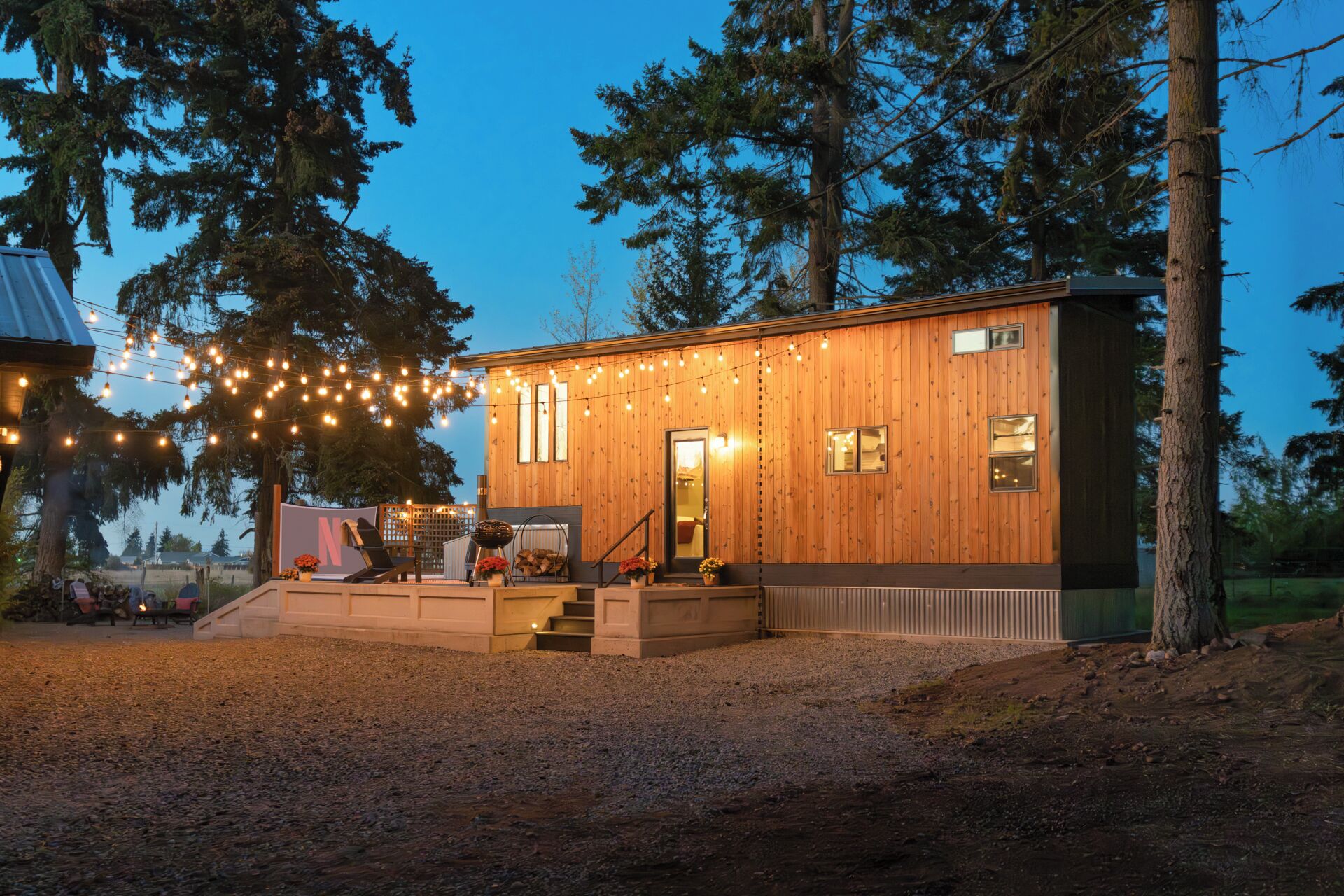 A wooden cabin with a porch, string lights, and a view of the surrounding forest.