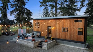 Una cabaña de madera con terraza, mobiliario exterior e iluminación con luces colgantes.