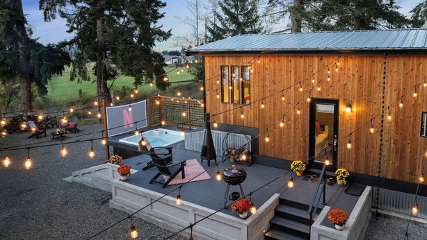 Una cabaña de madera con jacuzzi, mobiliario exterior y luces colgantes.