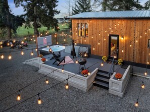 Una baita di legno con vasca idromassaggio, area salotto esterna e luci decorative.