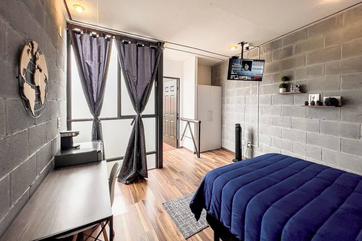 Un dormitorio moderno con cama, escritorio y televisor montado en la pared.