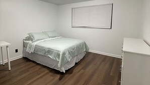 Un dormitorio con una cama, una mesita de noche, una ventana con persianas y una lámpara en el techo.
