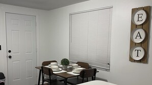 Una cocina moderna con encimera blanca, una mesa de comedor preparada con platos y una planta en maceta, y un letrero en la pared que dice 'EAT'.