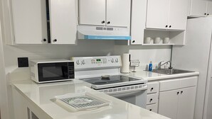 Una cocina moderna con armarios blancos, microondas, estufa y pileta. Hay taburetes en la isla y un cartel que indica que la cocina está cerrada.