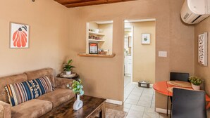A cozy living room with a brown sofa, a coffee table, and a small dining area with a red table and chairs. There is a shelf with books and a framed picture on the wall. - Private Serene Escape with Patio and Fenced Yard in West Sedona (Sedona)