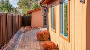 A house with a brick pathway leading to a wooden door, surrounded by a wooden fence and a small garden with red foliage. - Private Serene Escape with Patio and Fenced Yard in West Sedona (Sedona)