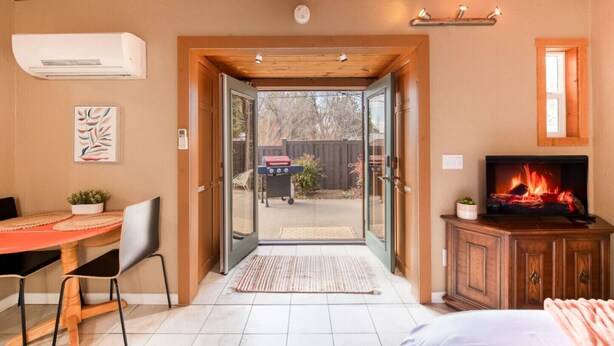 A room with a wooden ceiling, a television, a fireplace, a door leading outside, and a small table with a chair. - Private Serene Escape with Patio and Fenced Yard in West Sedona (Sedona)