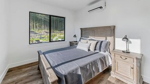 A bedroom with a large window, a bed, a nightstand, and a dresser. - High-end, convenient, new build! (Juneau)