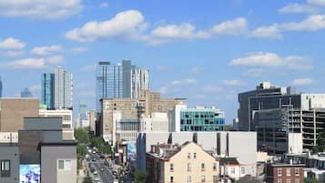 Un paysage urbain mêlant bâtiments modernes et bâtiments plus anciens, un ciel dégagé et une rue animée où circulent des voitures et des piétons.
