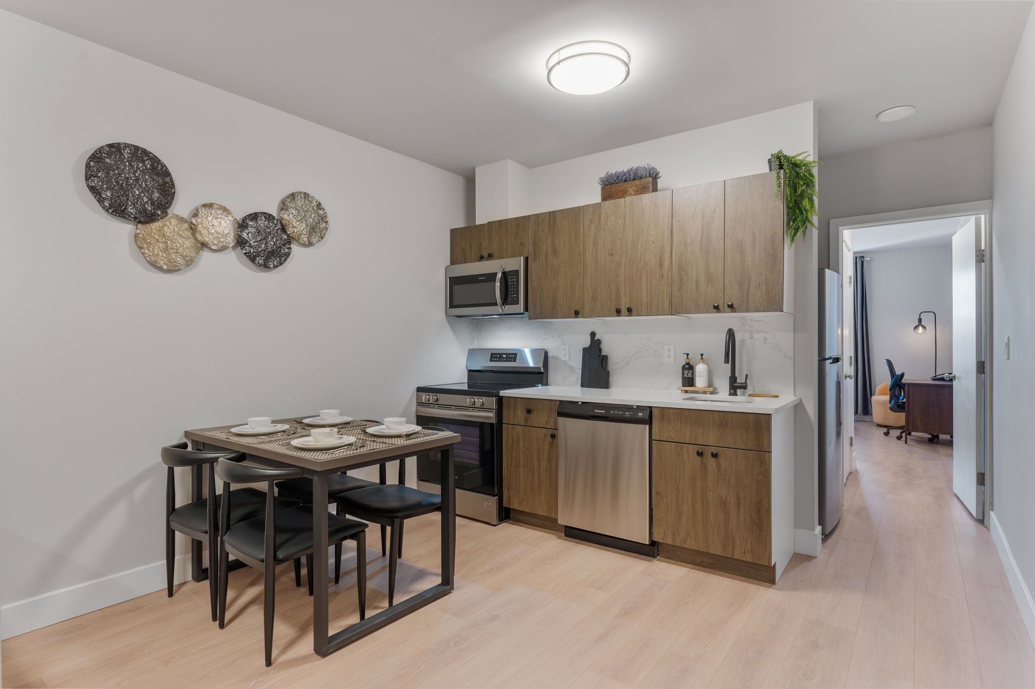 A modern kitchen with wooden cabinets, a built-in microwave, and a dishwasher. There is a dining table with chairs and a decorative wall piece.