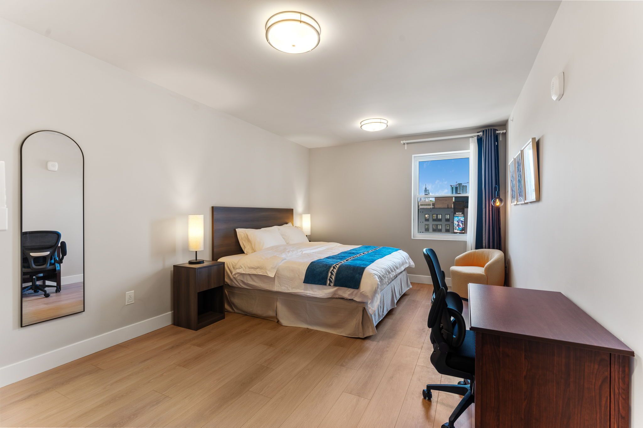 Una habitación de hotel moderna con cama, escritorio, silla y un espejo grande.