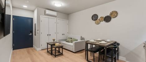 Una sala de estar moderna con un sofá gris, una mesa de comedor con sillas y un televisor montado en la pared.