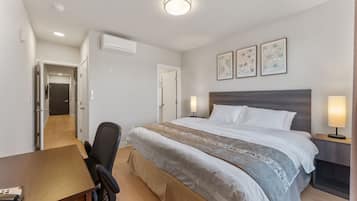 A hotel room with a bed, bedside table, lamp, and a desk with a chair.