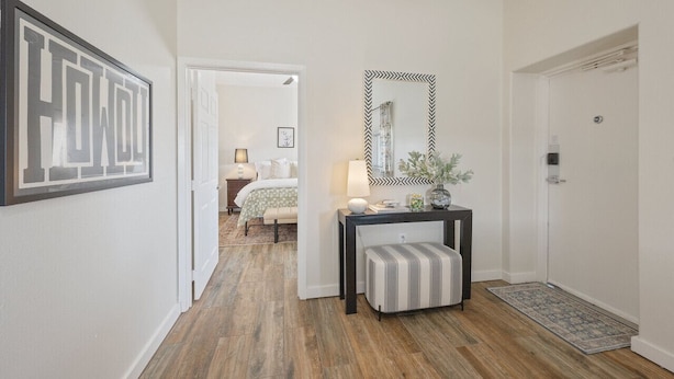 A hallway with a wooden floor, a white door, a console table with a mirror, and a framed artwork on the wall.