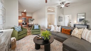 A modern living room with a sofa, chairs, a coffee table, and a kitchen in the background.