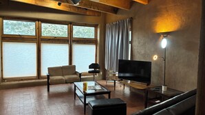 A spacious living room with a large window, a ceiling fan, a flat-screen TV, a sofa, a coffee table, and a lamp. - Charming 1.5 Bedrooms, 1600 sq. Ft Guest House Views/Yard W/D High Ceilings  (Santa Fe)