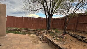 A backyard with a stone patio, a wooden fence, and a tree. - Charming 1.5 Bedrooms, 1600 sq. Ft Guest House Views/Yard W/D High Ceilings  (Santa Fe)