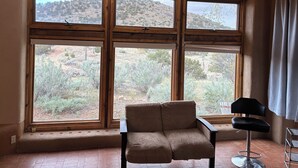 A room with large windows, a beige armchair, and a black bar stool. - Charming 1.5 Bedrooms, 1600 sq. Ft Guest House Views/Yard W/D High Ceilings  (Santa Fe)