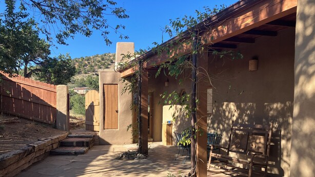 A courtyard with a stone floor, a wooden fence, and a covered seating area with chairs and a table. - Charming 1.5 Bedrooms, 1600 sq. Ft Guest House Views/Yard W/D High Ceilings  (Santa Fe)