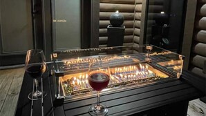 Une table dont le plateau est en verre, avec une cheminée allumée, deux verres à vin et un élément décoratif en pierre au centre.
