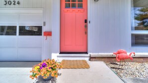 A white house with a bright pink door, a mailbox, and a flower pot on the front porch. - Walk to Beach, Ping Pong, King Beds, Sleeps 6 (Muskegon)
