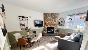 A living room with a stone fireplace, a television, a dining table with chairs, and a sofa. - Three Peaks Getaway - sleeps 4 (Canmore)