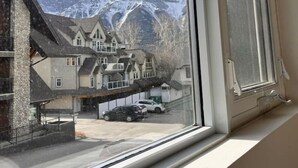 A hotel room with a large window overlooking a mountainous landscape and a parking area. - Three Peaks Getaway - sleeps 4 (Canmore)