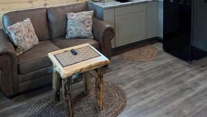 A cozy cabin interior with a wooden ceiling, a kitchen area with a sink and refrigerator, a brown leather sofa with patterned cushions, and a small wooden table. - Bear Top Junior Small Cabin w EV Charger

 (Cosby)