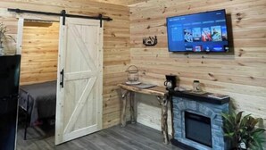 A cozy room with a wooden ceiling, a TV mounted on the wall, a fireplace, and a sliding barn door. - Bear Top Junior Small Cabin w EV Charger

 (Cosby)